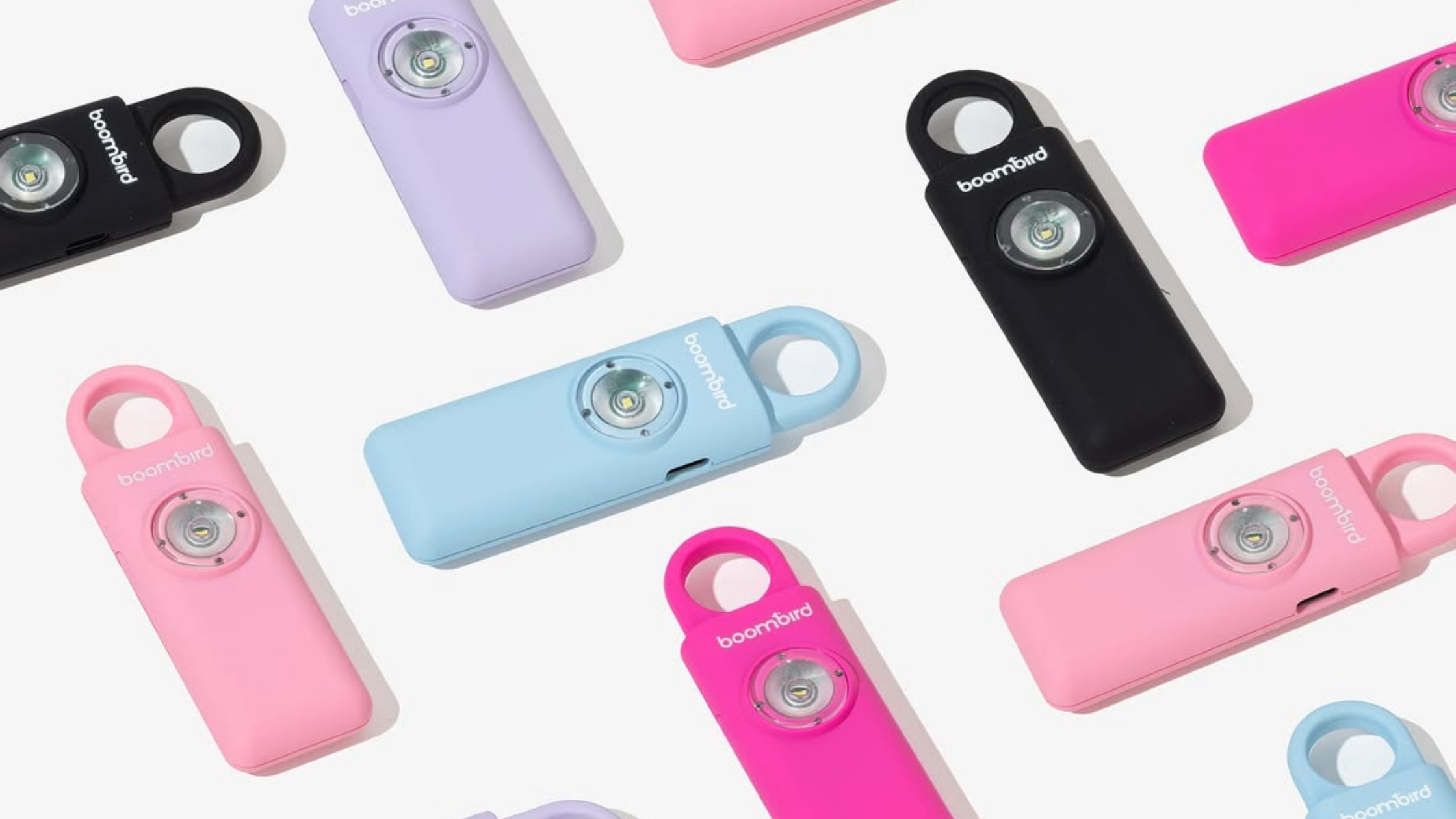 Multiple BoomBird personal safety alarm keychains in different colors (black, pink, purple, blue) arranged on a light background, highlighting their compact design with LED flashlight and keyring loop.